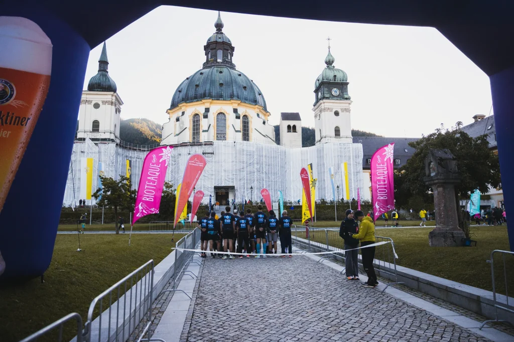 Blick unter dem Startbogen auf eine Gruppe in gleichen Shirts in der Startgasse vor dem Kloster Ettal.