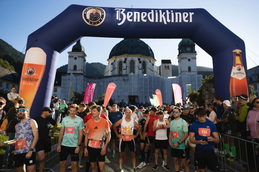 Eine große Laufgruppe wartet unter dem Startbogen vor dem Kloster Ettal.