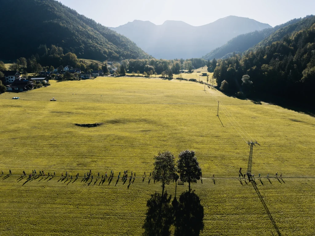 Luftaufnahme von Laufenden auf einem Wiesenweg zwischen bewaldeten Bergen.