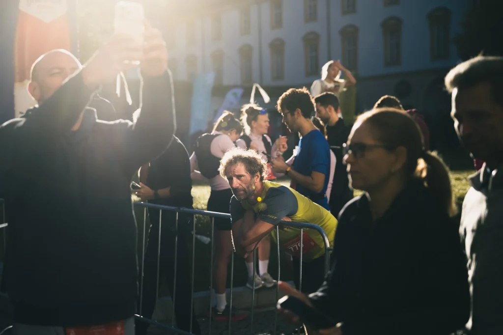 Ein Teilnehmer im gelben Shirt lehnt zwischen anderen Menschen an einer Absperrung im Sonnenlicht.