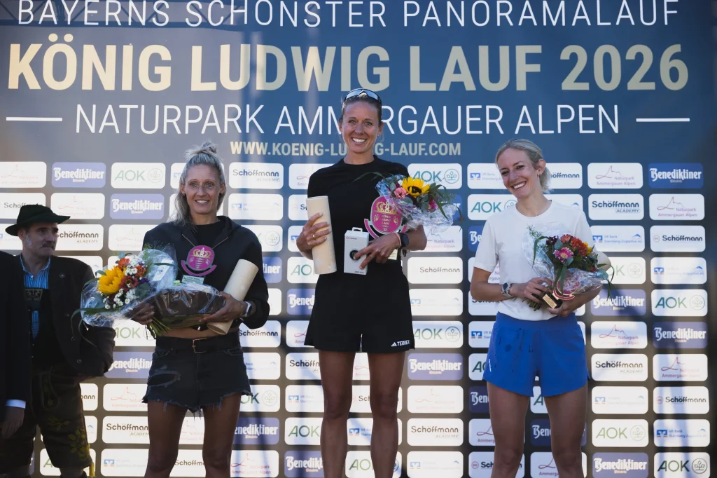 Drei lächelnde Läuferinnen mit Blumen und Auszeichnungen bei der Siegerehrung 2026.