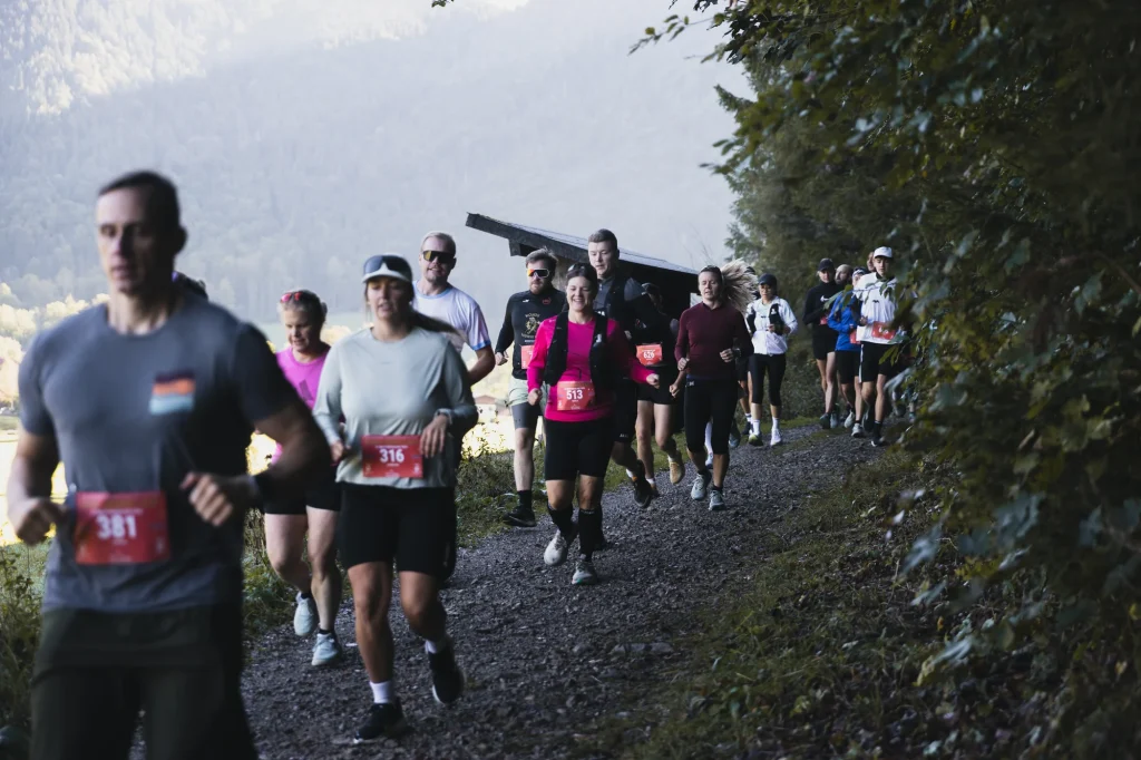 Eine Laufgruppe auf einem schattigen Weg; zwischen den Teilnehmenden lächelt eine Läuferin im pinken Shirt.